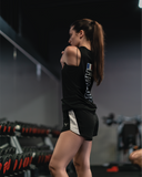 Femme portant le débardeur Blaze Boule de Feu noir synthétique en train de s’étirer les bras dans une salle de sport