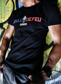 Homme portant le t-shirt Frenchy Boule de Feu noir en coton biologique avec logo bleu blanc rouge devant un mur de graffitis